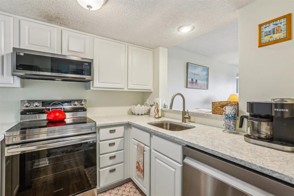 - Another kitchen view shows dishwasher, coffee maker and modern sink with ample counter space  
- Stainless steel finishes blend with bright décor for a clean look  
- Perfect for vacation cooking convenience  
