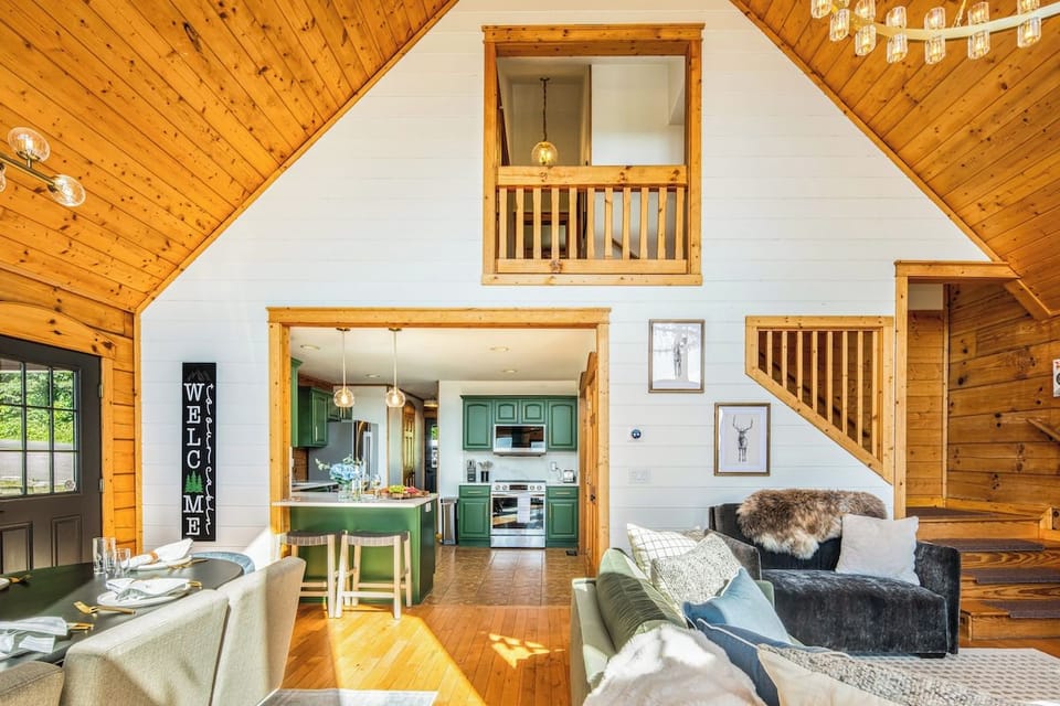 From the A-frame wall of windows, enjoy a sweeping view of the open living, dining, and kitchen spaces — all framed by the mountains beyond.