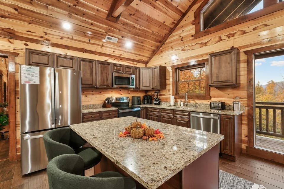 rustic kitchen with granite island and stainless steel appliances overlooking autumn trees