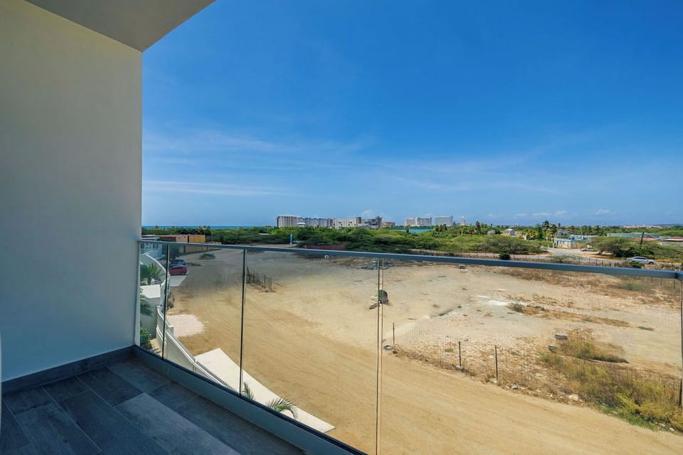 This sleek glass-railed balcony offers sweeping views of the surrounding neighborhood, open fields, and distant cityscape under bright blue skies—a peaceful spot to enjoy open-air relaxation.