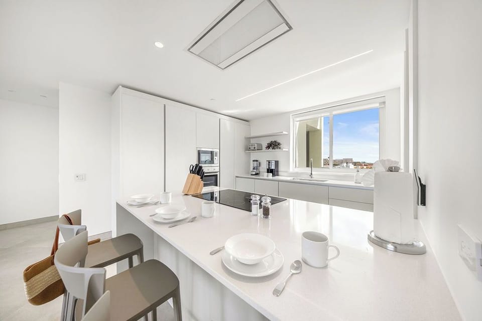 Picture yourself preparing meals in this bright, modern kitchen with sleek countertops, integrated appliances, and sunlight streaming through large windows—your perfect space for cooking and gathering.