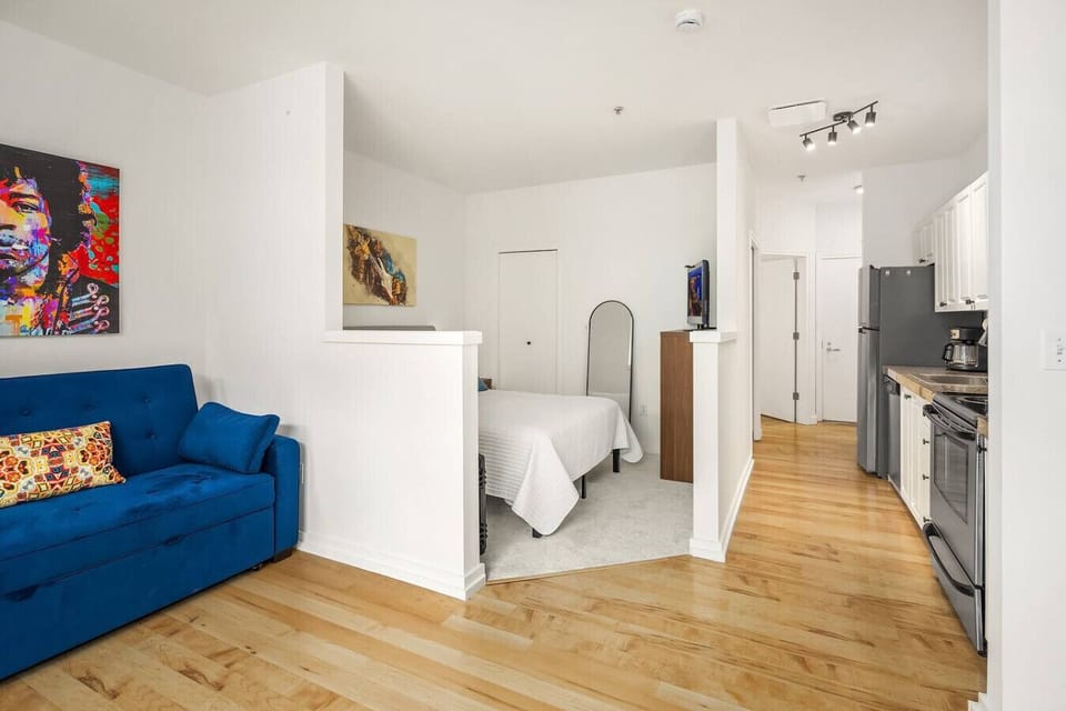 Open layout with a cozy living area, hardwood floors, modern furnishings, and a peek into the inviting bedroom.