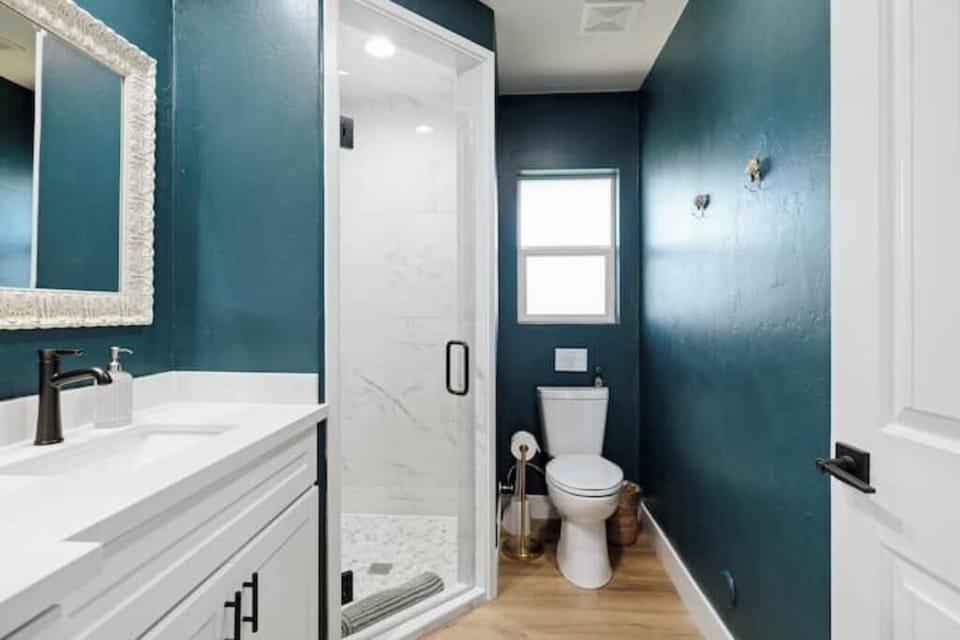 Bathroom with glass walk-in shower, toilet and teal walls.