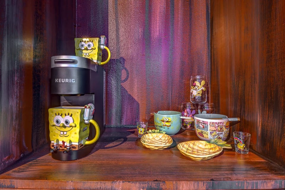 A keurig coffee maker with spongebob-themed mugs and dishes on a wooden shelf.