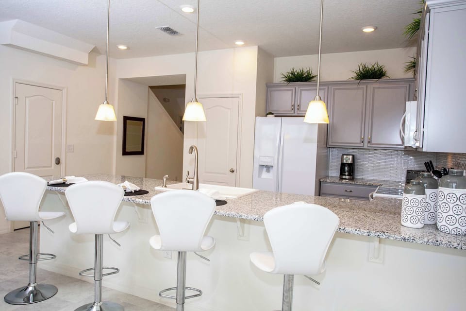Modern open-concept kitchen with gray cabinetry, granite island, and a row of white bar stools-perfect for casual meals and socializing.