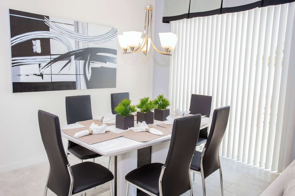 Dining space features bold black-and-white art, a white table, and natural light from vertical blinds-stylish, inviting dinners.