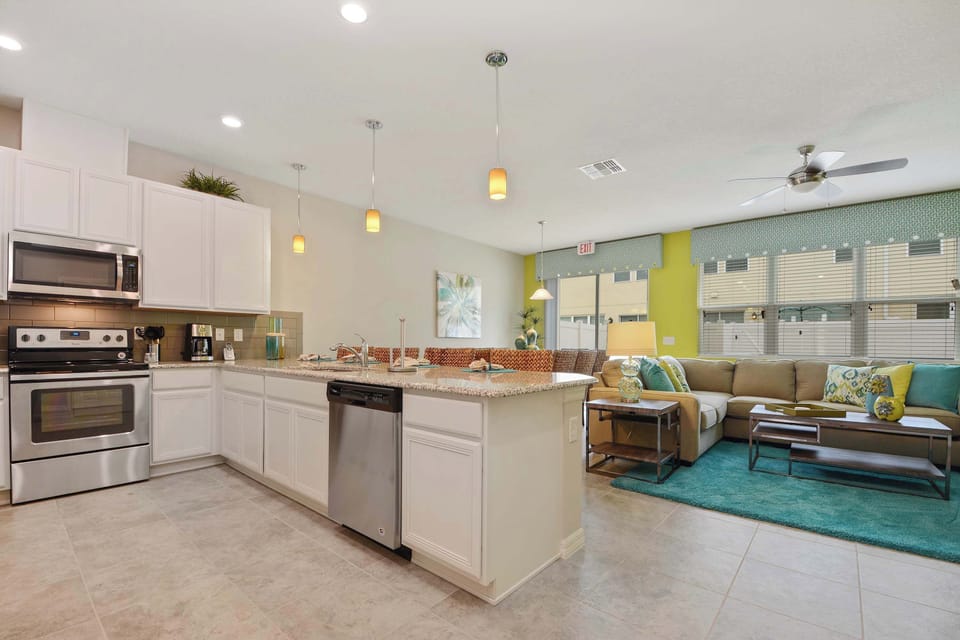 Open-concept kitchen flows into the colorful living room, with stainless appliances, granite island, and pendant lighting for a fresh, modern coastal vibe.