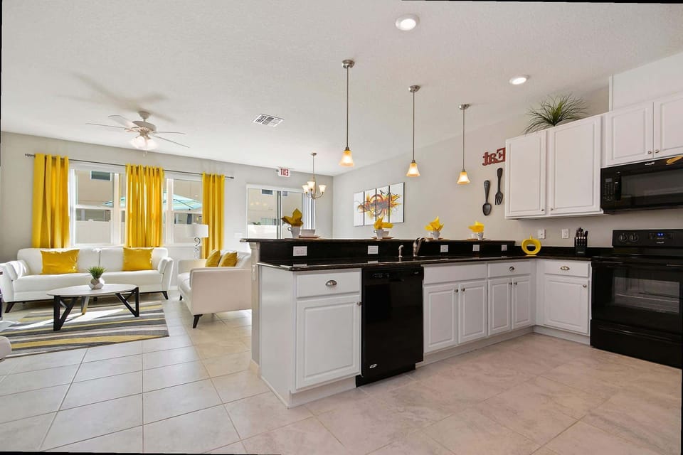 Whip up meals in the sleek open kitchen, boasting white cabinetry, black appliances, and a breakfast bar that overlooks the sunny living area with cheerful yellow accents.