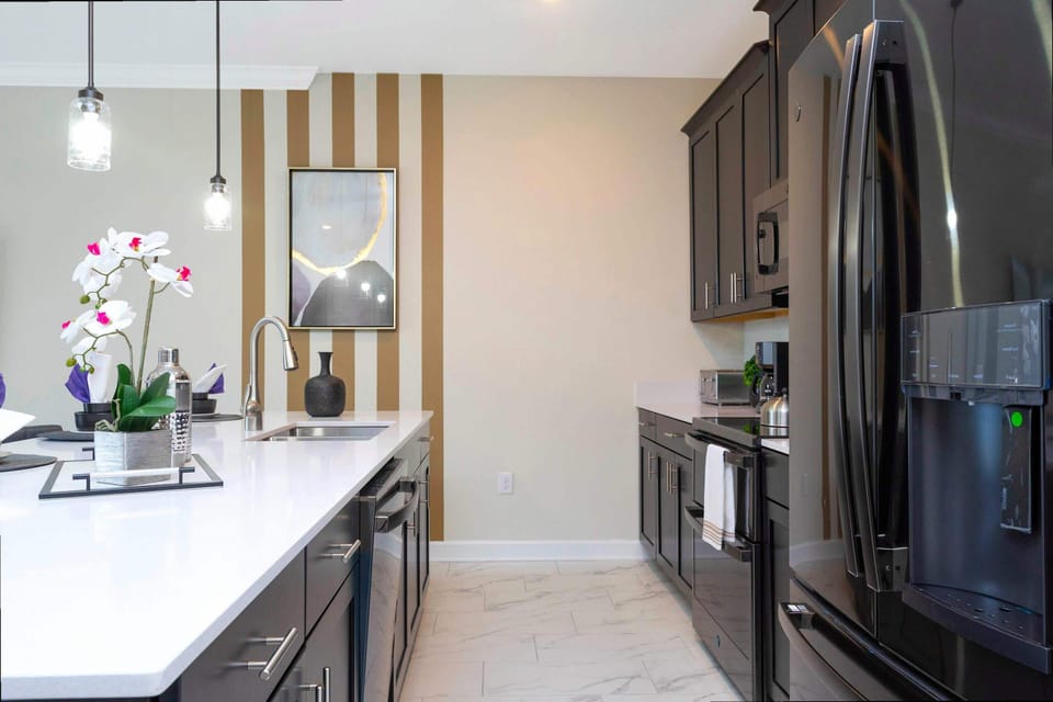 Discover the chef's dream kitchen with sleek black cabinets, stainless steel appliances, and a spacious quartz island under glass pendant lights-accent wall stripes add a playful modern twist!
