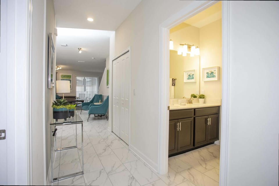 Discover seamless flow from the marble-effect foyer into a bright bathroom featuring a dark wood vanity and crisp white countertops - fresh and inviting!
