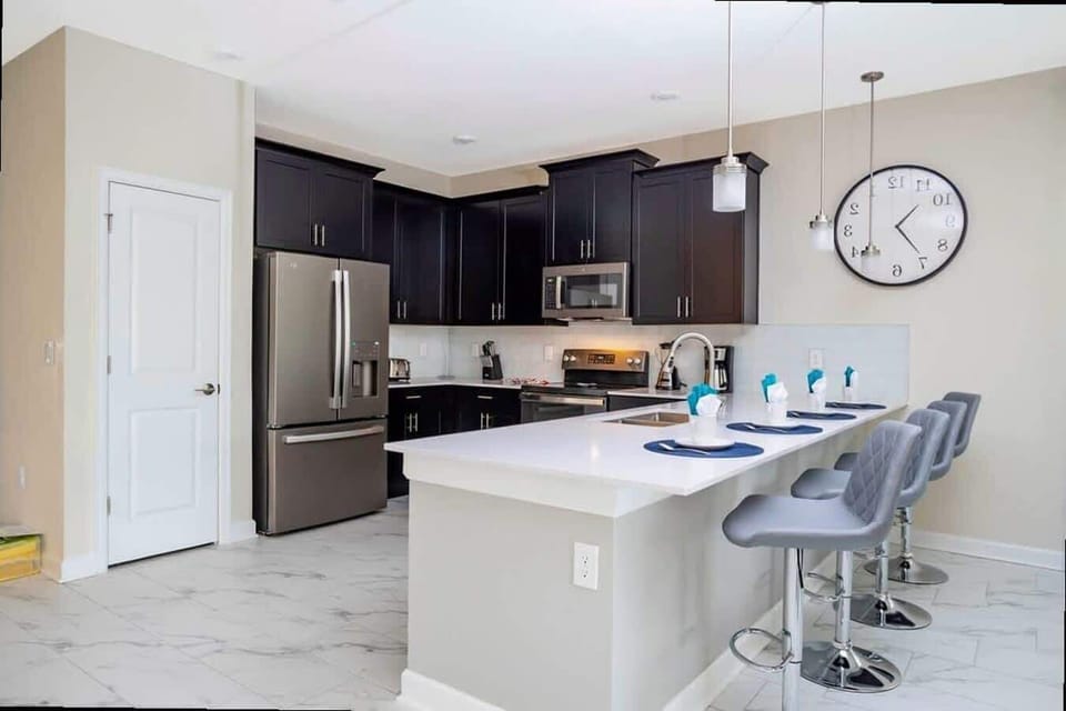 Gather in this sleek kitchen with dark wood cabinets, stainless steel appliances, and a spacious quartz island with seating for four. Pendant lights and marble-look floors add a modern, airy vibe-perfect for whipping up family meals!