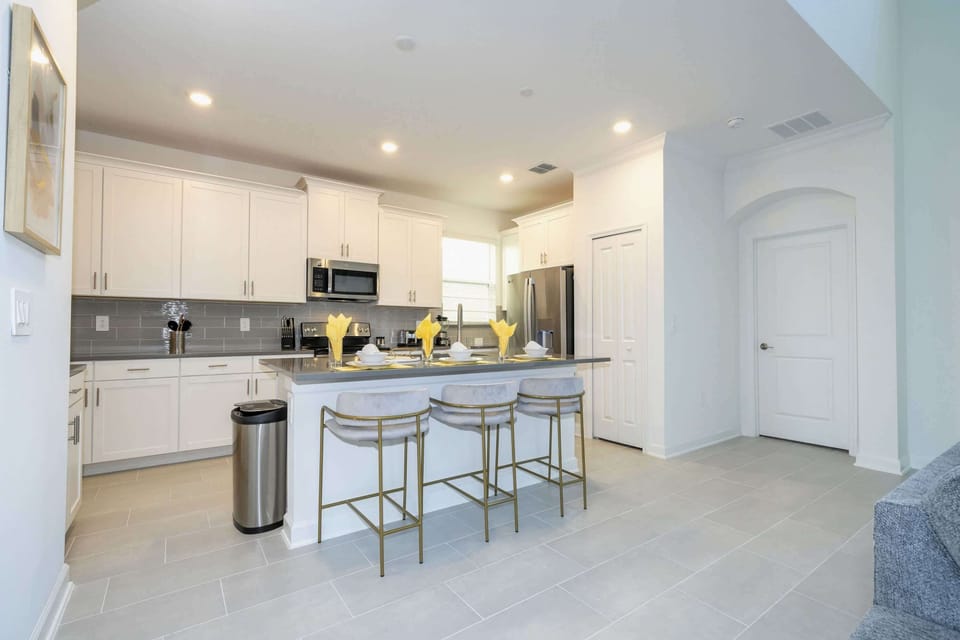 Enjoy bright mornings and casual breakfasts in this modern kitchen with a large island, elegant white cabinetry, and dazzling gold-accented bar stools!