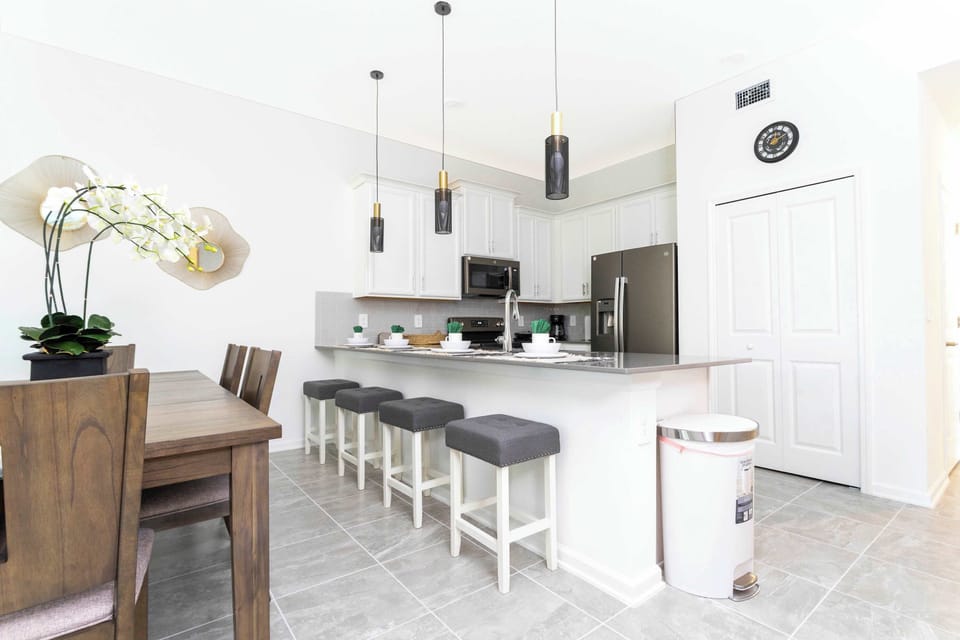 Sleek chef's kitchen meets dining-white cabinets, statement pendants, and a long breakfast bar with four stools. Perfect for morning coffee or family meals.