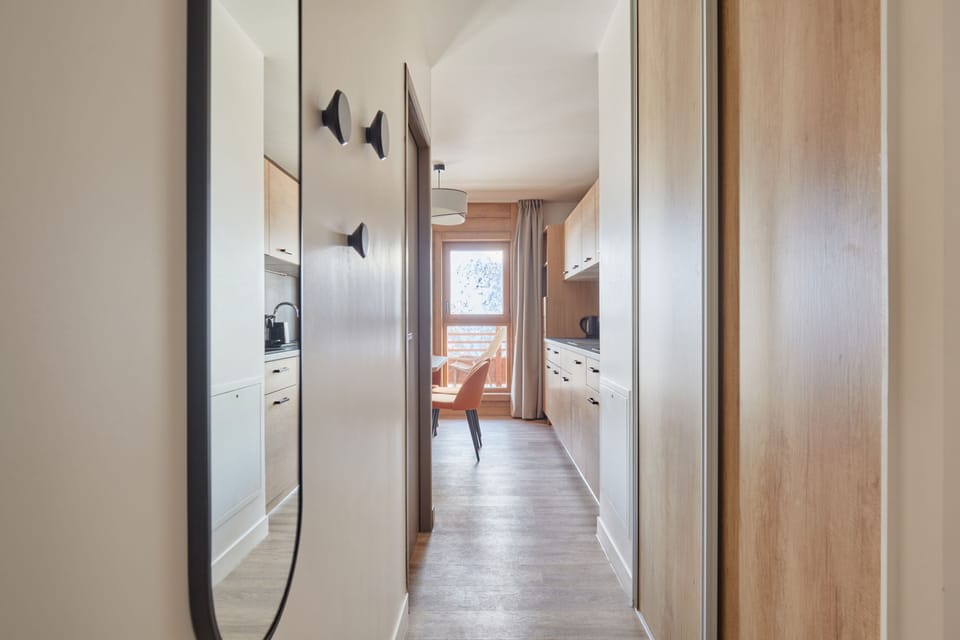 Hallway with a mirror, coat hooks, and light wood cabinetry — a practical entry point connecting the living spaces.
