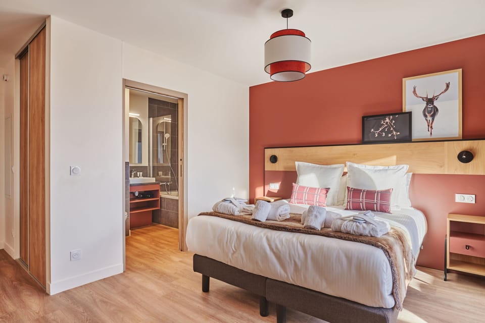 Double bed with warm red walls and wooden headboard — bed linen is included in every stay.