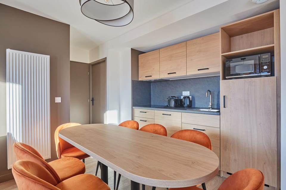 Kitchenette with light wood cabinetry and black countertop — stovetop, microwave, fridge, and dishwasher all included.