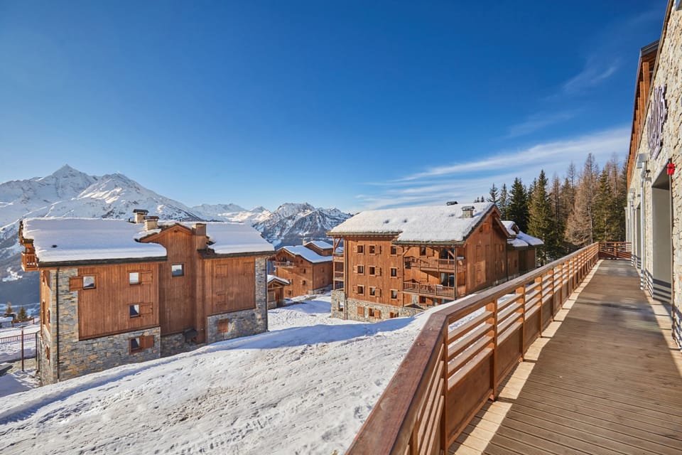 Snow-covered chalets line the walkway outside, with the ski runs of La Rosière rising in the background.