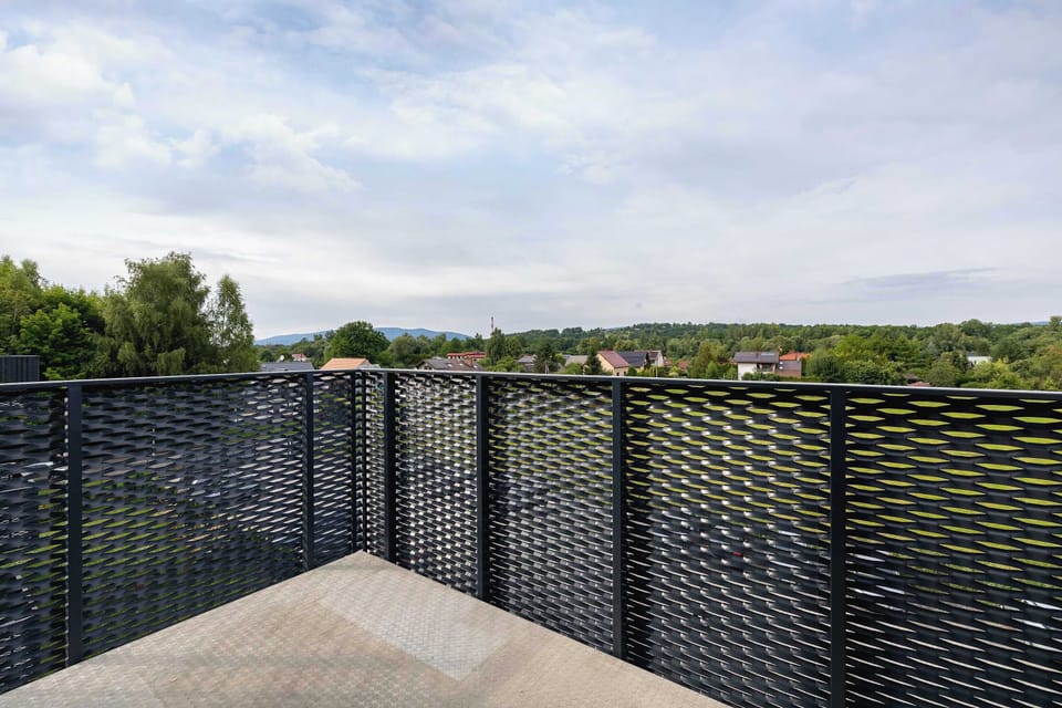 A private balcony with black mesh railing and a view of the greenery below.

