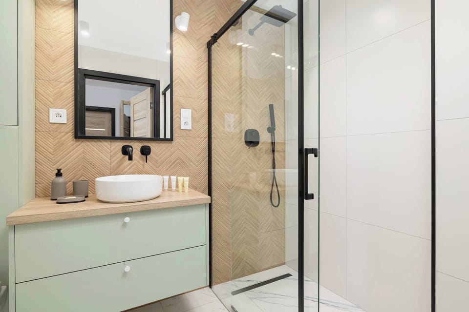 A well-lit bathroom with a walk-in shower, black fixtures, and modern wood finishes.

