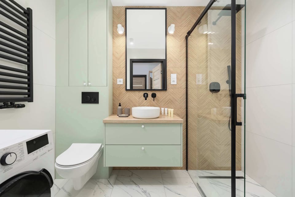 A walk-in shower with beige tiles and a glass enclosure, next to a toilet and washing machine.
