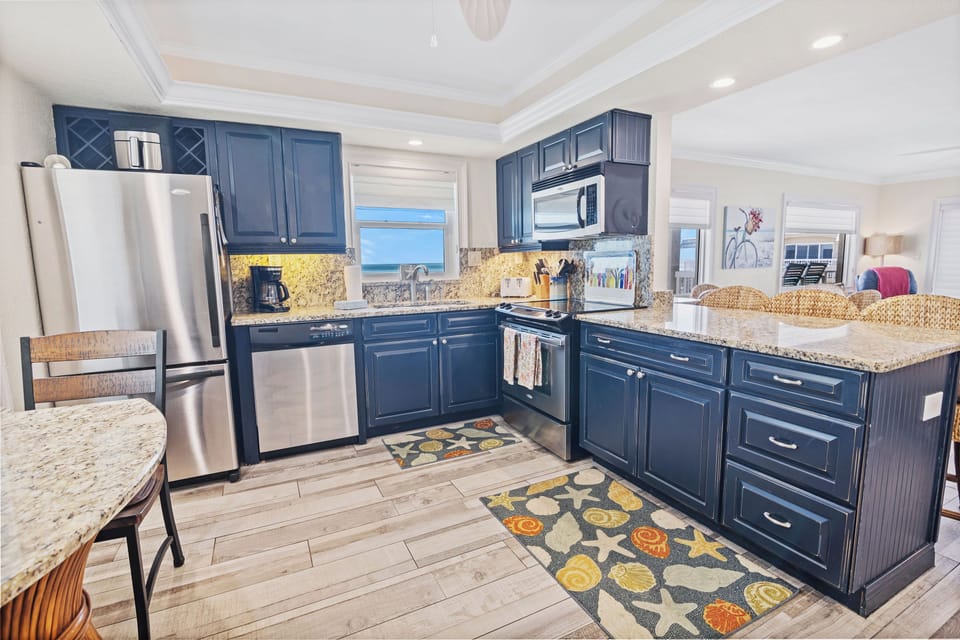 Enjoy cooking with a view in this fully equipped coastal kitchen featuring granite countertops, stainless steel appliances, and nautical accents—perfect for your relaxing beach getaway.