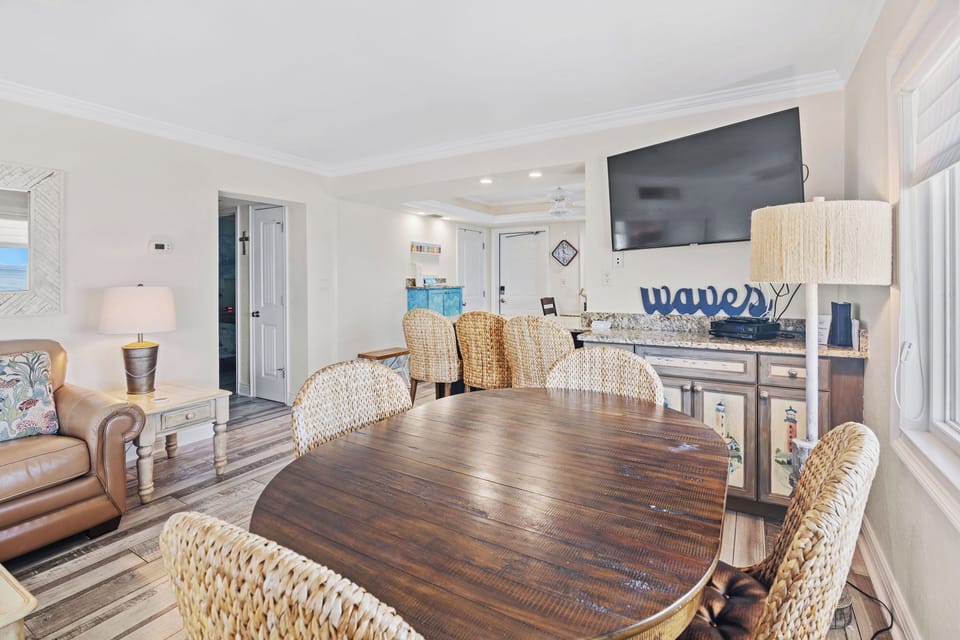 Enjoy relaxed beach stays with this inviting dining space, featuring wicker chairs, coastal décor, and a large TV. Perfect for sharing meals and making memories after a day by the ocean.