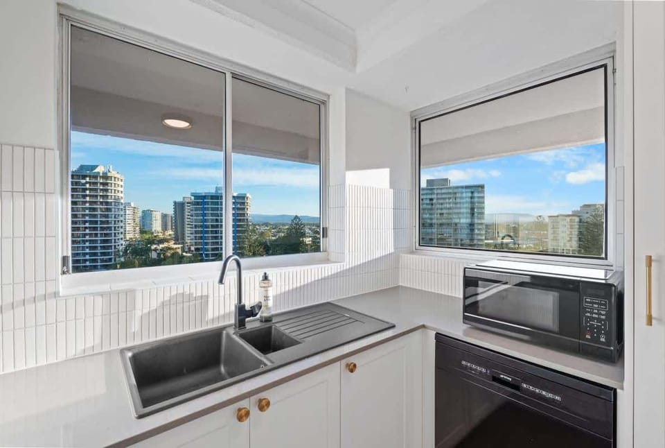 Bright and practical kitchen with two open windows, full-size sink, microwave, and dishwasher.