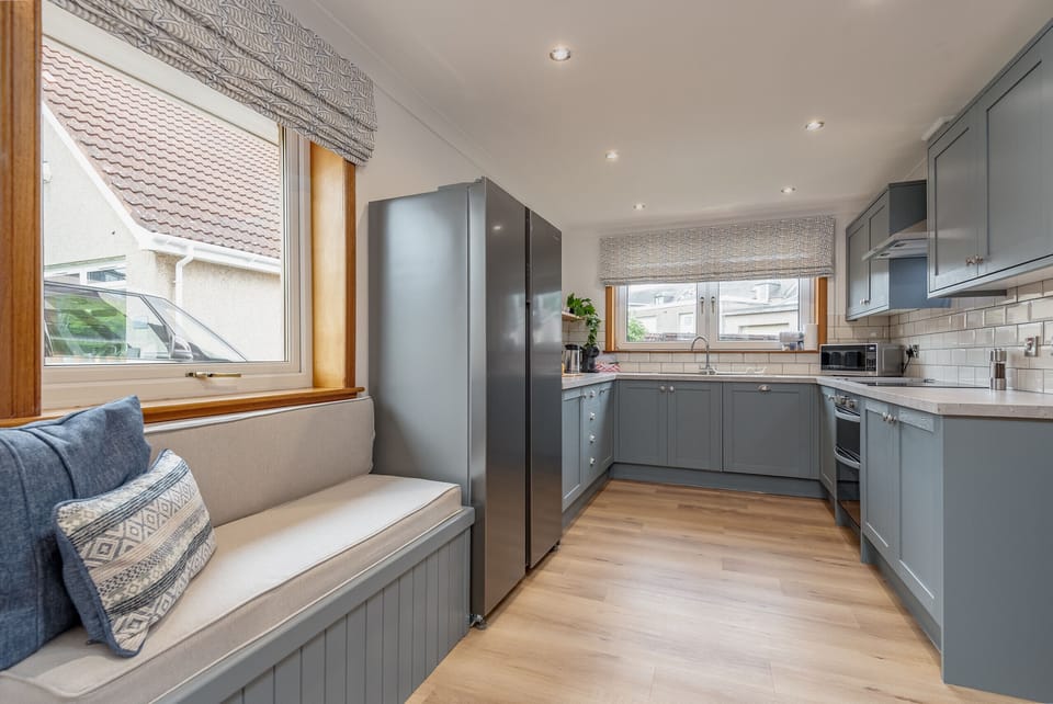 Bright kitchen with blue cabinetry, stainless steel fridge, and a cushioned bench under the window.