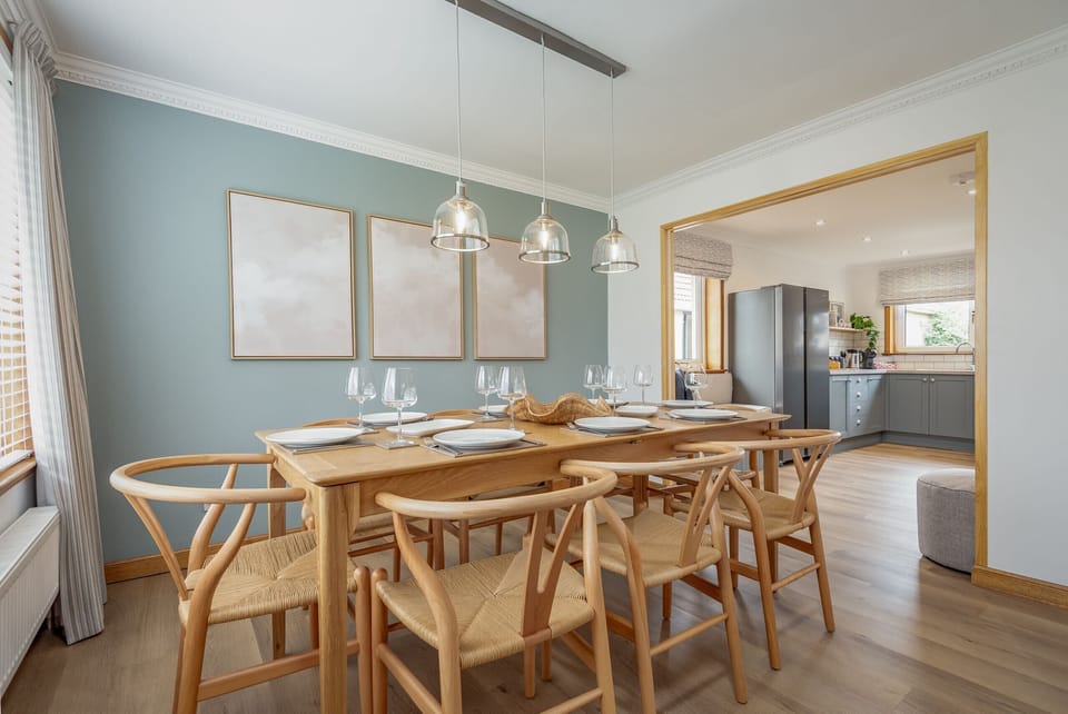 Contemporary dining room with wooden table and chairs, pendant lights, and open access to the kitchen.