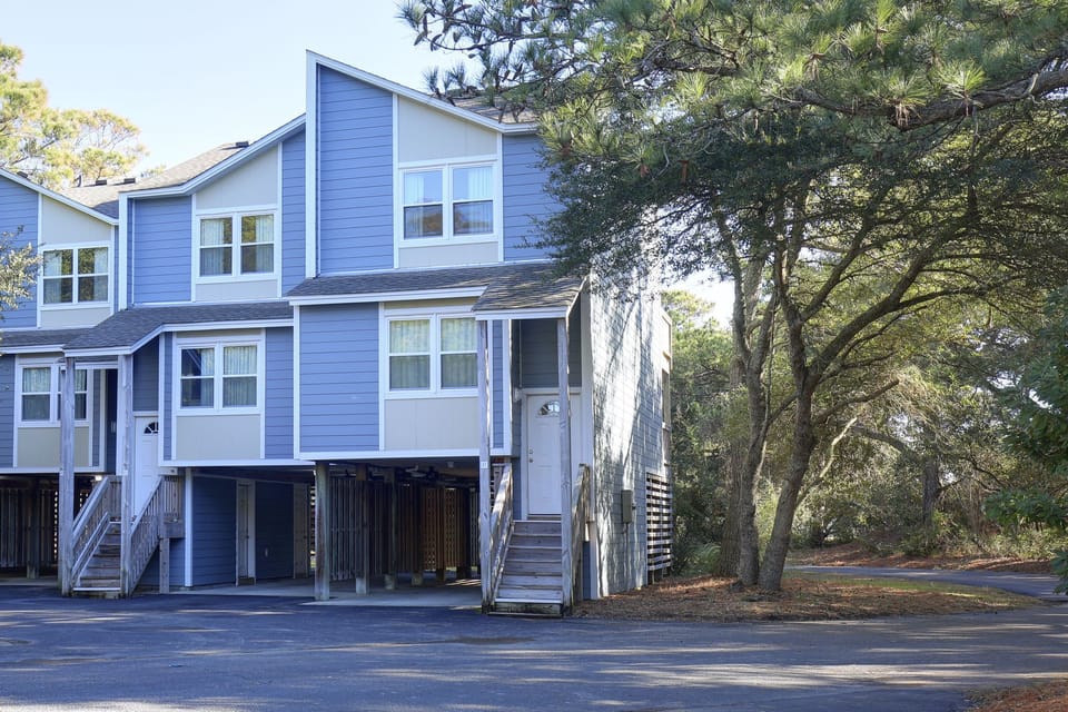 This charming 1BR condo at Ocean Pines Resort features a welcoming exterior, nestled among lush trees, offering a peaceful retreat near the beach.