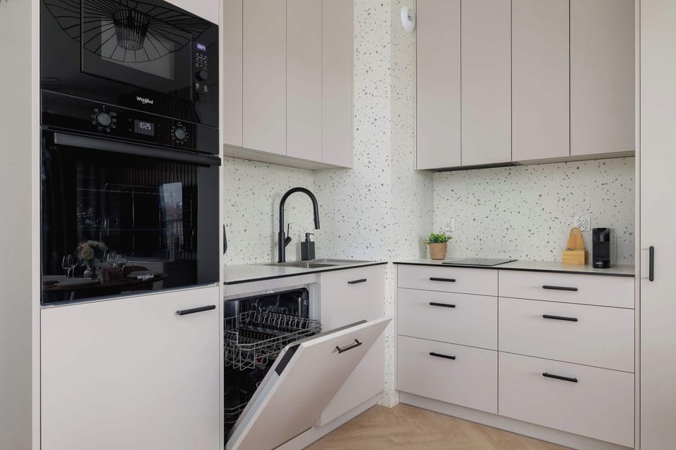 A modern kitchenette with bright cabinets, a built-in oven and microwave, and an open dishwasher looks elegant and functional.