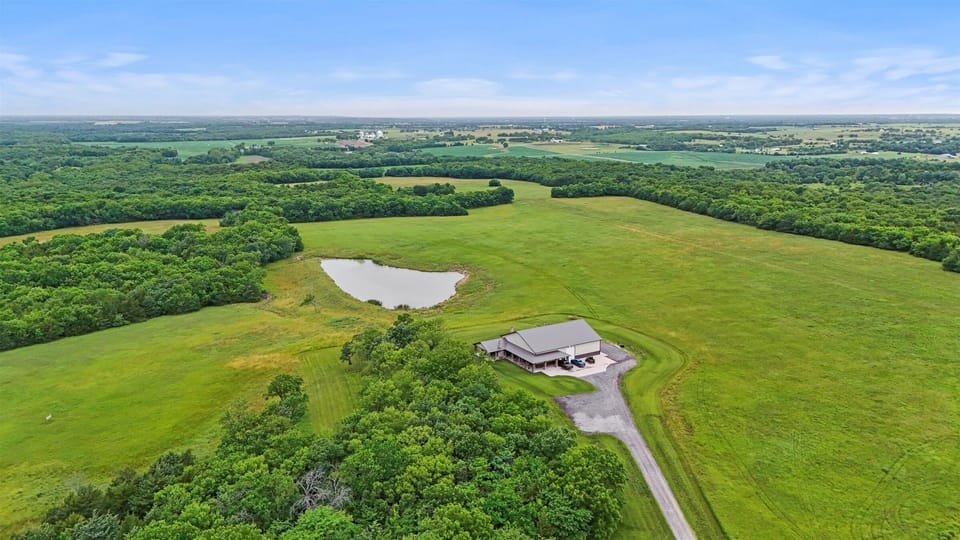 Expansive aerial view of Wilderness Lodge set on 440 private acres, featuring rolling hills, wooded trails, and a peaceful on-site stocked fishing pond.