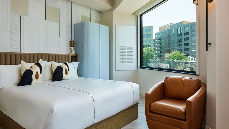 Bright room with large bed, leather chair, and city view window