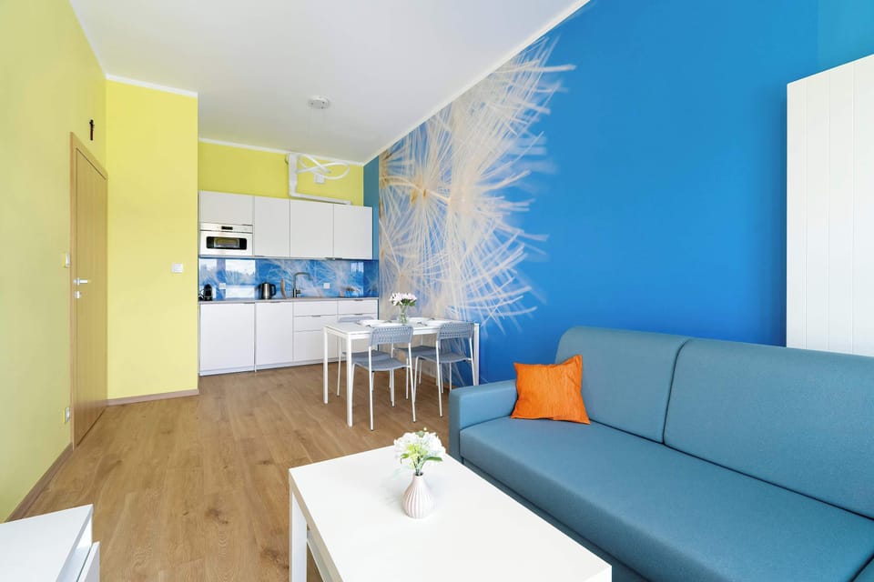 A wide view of the living and kitchen area with blue accent walls, a gray sofa, and a small breakfast table.