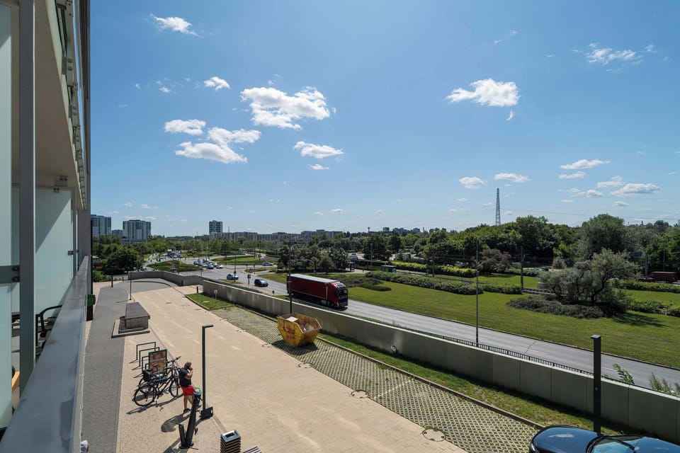 A second balcony view showing a longer stretch of river, paths, and a road with cars passing by.