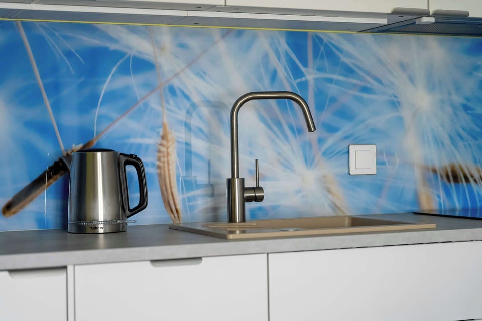 A close-up of the kitchen sink area, showing a kettle, faucet, and glossy blue wall paneling with a light pattern.