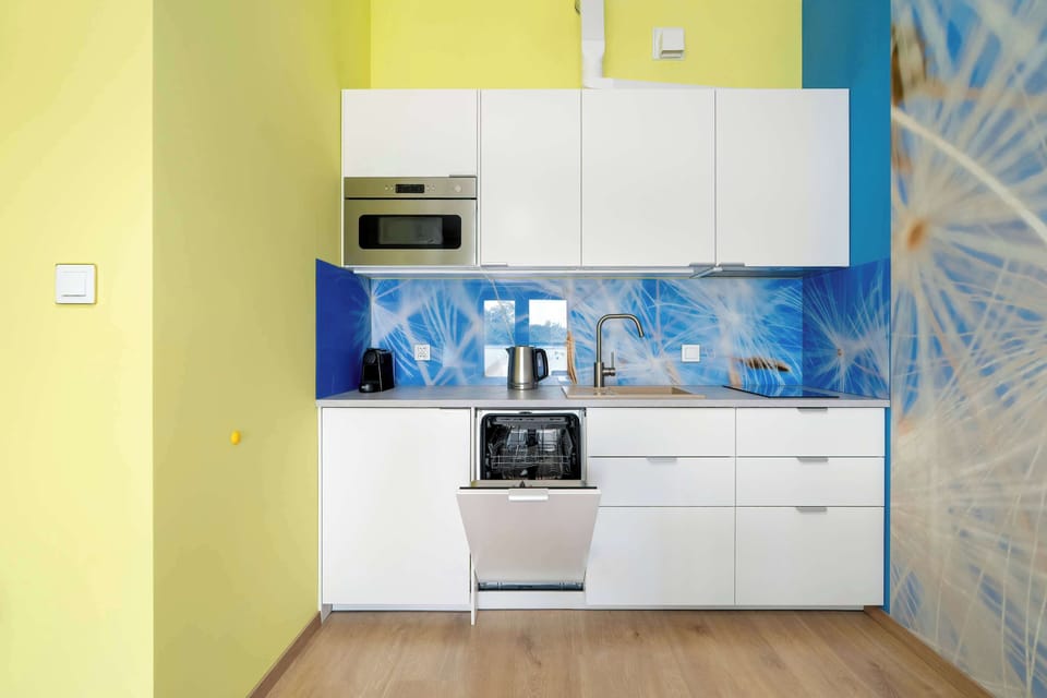 A stylish kitchenette with white cabinets, an open dishwasher, and a blue-and-white wall design against yellow walls creates a functional and aesthetic space for everyday use.