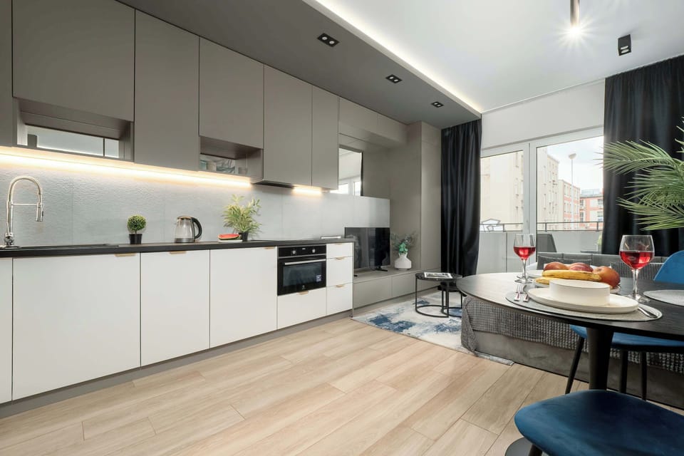 A contemporary kitchen with sleek white cabinets and a grey backsplash, viewed from a side angle.

