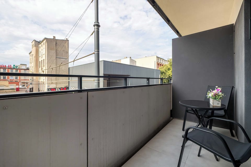 A balcony with a small table and chair, overlooking nearby buildings.

