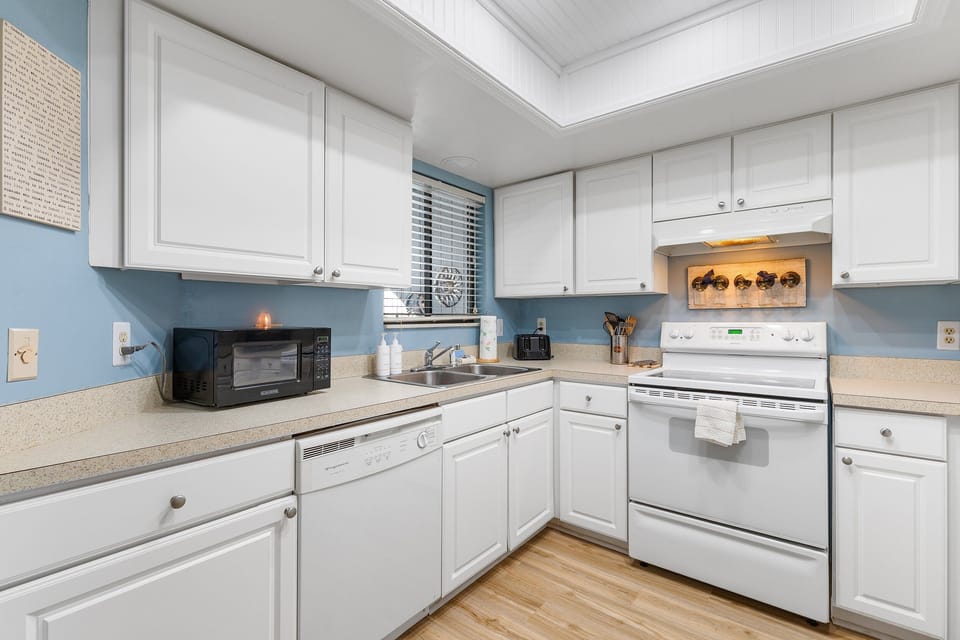 Whip up seaside meals in this fully equipped beach-style kitchen featuring white cabinetry, modern appliances, and a cheerful coastal vibe—perfect for your beach getaway!