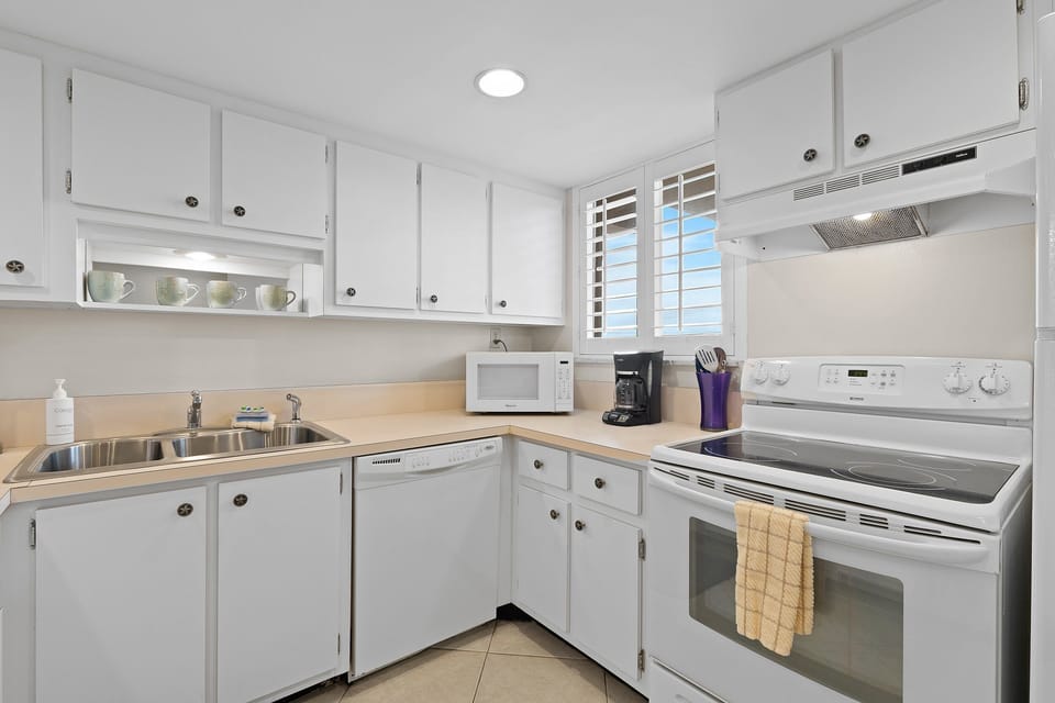 Cook up your favorite coastal meals in this bright, fully equipped beach kitchen featuring white cabinetry, modern appliances, and plenty of natural light for your seaside getaway.
