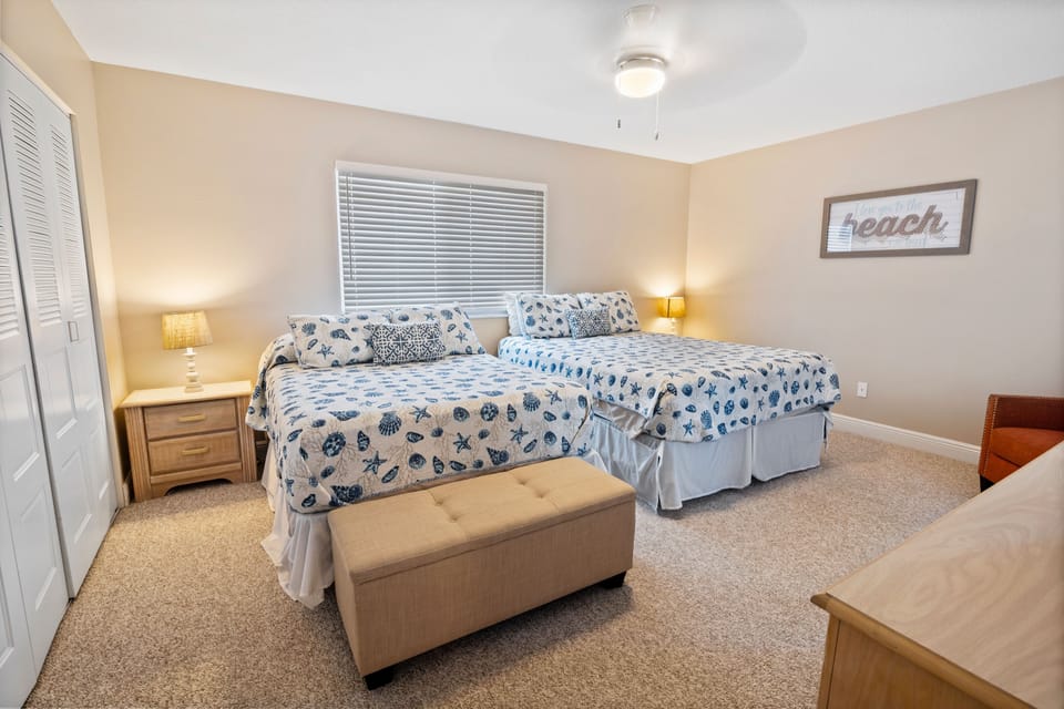 This inviting guest room features two plush beds with seashell-themed bedding, warm lighting, and beach-inspired décor—perfect for relaxing after a fun day by the ocean.