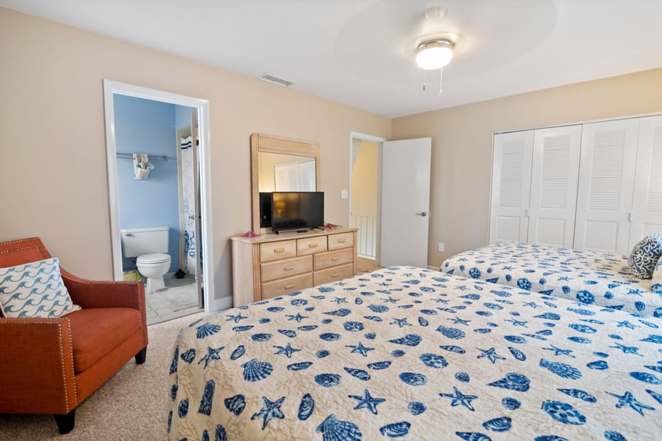 Relax in this bright beach-inspired guest bedroom featuring twin beds, seashell bedding, and a private bath. Perfect for a coastal getaway filled with comfort and ocean charm.