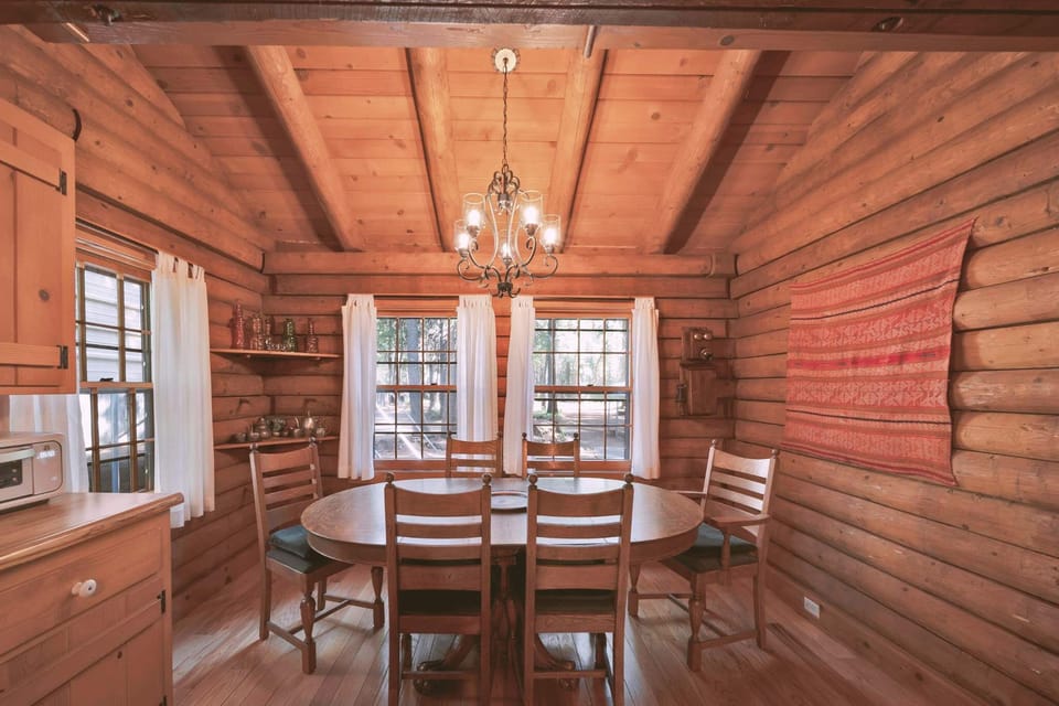 Adjacent to the kitchen, the dining area invites you to gather around a solid wood table with seating for six. Surrounded by large paned windows, the room is bathed in natural light by day and softly lit by a charming chandelier in the evenings.