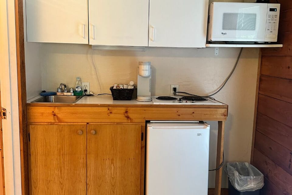 The room features a microwave, mini fridge, stovetop, and Keurig. 