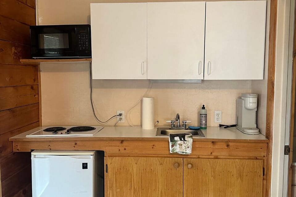 The room features a kitchenette with a mini fridge, microwave, sink, and Keurig.