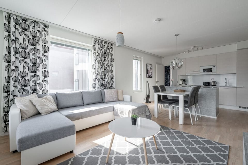 A bright and modern open-concept living space with a cozy corner sofa, fully equipped kitchen, and dining area—perfect for relaxing or entertaining.