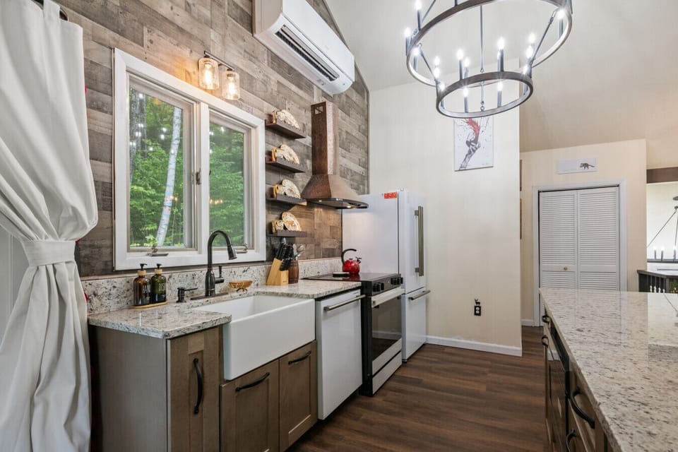 Modern chalet kitchen with granite countertops, farmhouse sink, copper range hood, and mini split air conditioning to keep the upstairs cool and comfortable year-round. Forest views and spacious prep space for family meals.