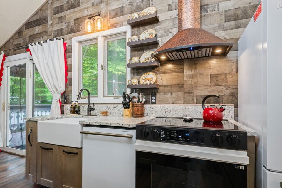 Rustic chalet kitchen with granite countertops, farmhouse sink, copper range hood, full-size appliances, and forest views. Fully equipped for family meals with direct access to the wraparound deck.