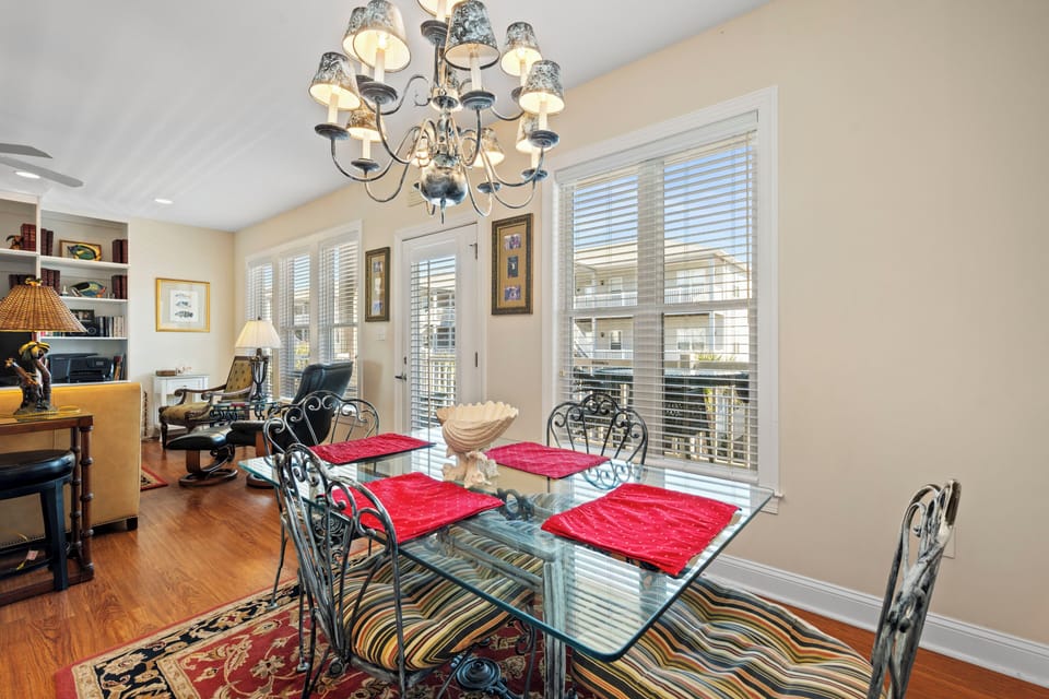Your elegant dining room features a stunning glass table under an ornate chandelier, with large windows flooding the space with natural light.